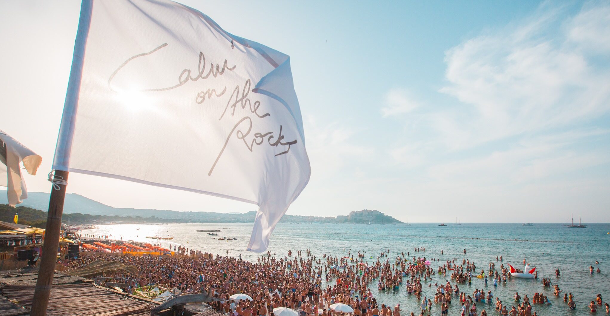 View of Calvi On The Rocks flag waving on the beach with people dancing - credits Calvi On The Rocks - Calvi On The Rocks 2023 - Lineupping.com