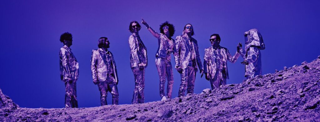 Arcade Fire band members standing up in the desert - credits Arcade